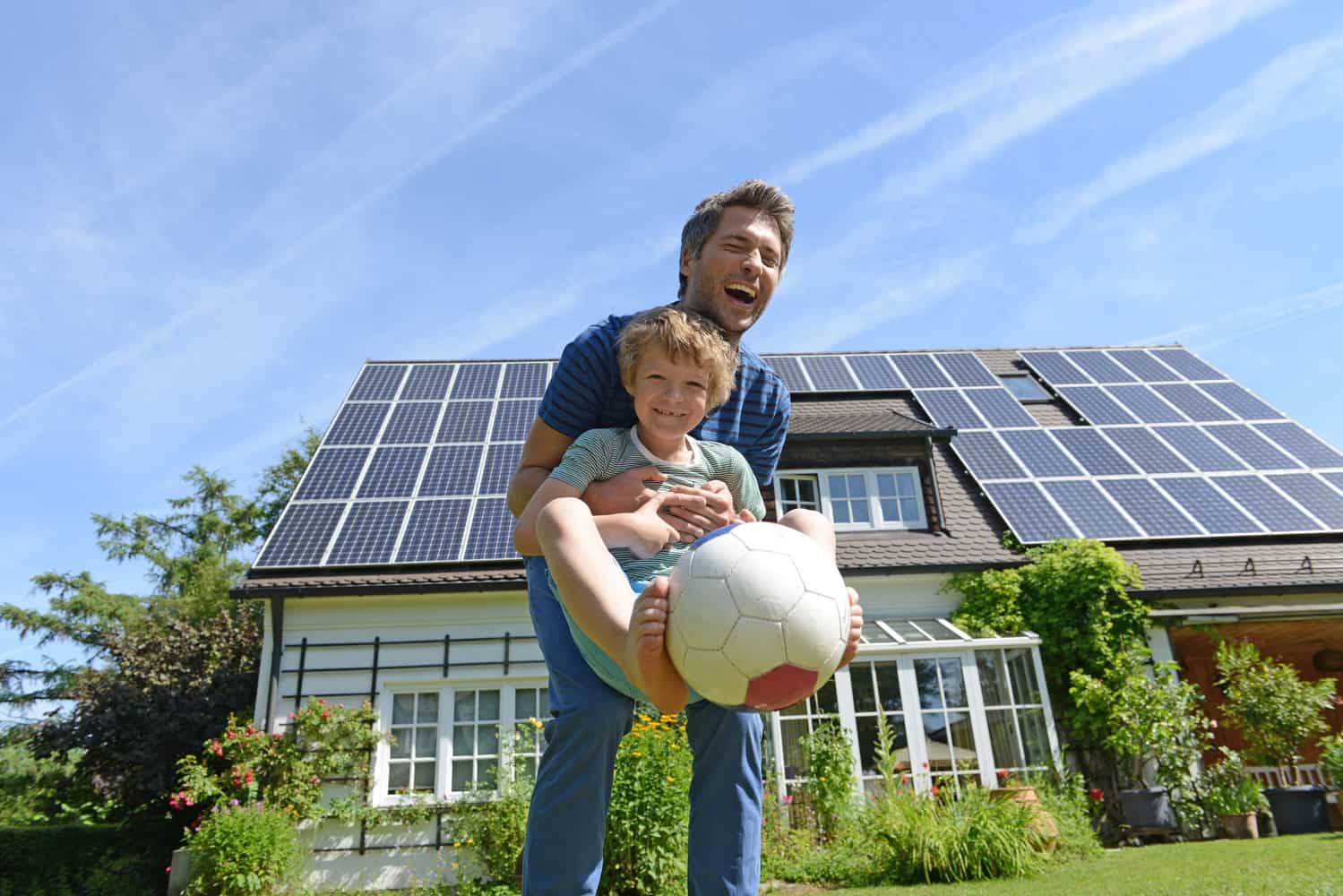 Familie vor einem Einfamilienhaus mit Photovoltaik-Anlage
